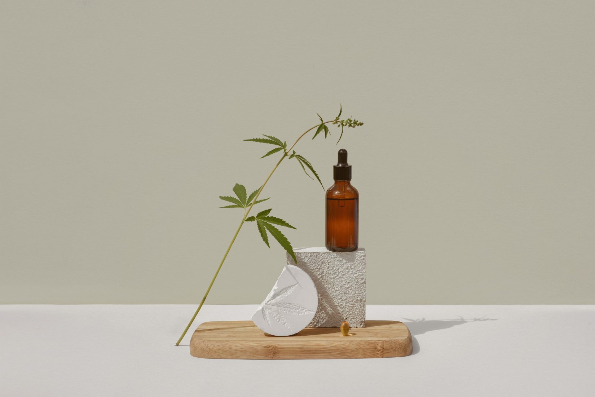 CBD oil in brown bottle with dropper and cannabis branch, hemp on podium Beige background